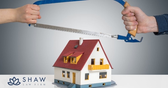 Two hands holding a saw over a fake house on a white table.